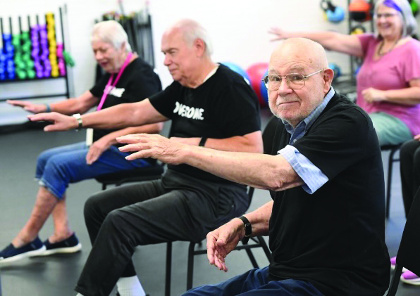 Man in a class with other seniors at a senior center, looking at the camera and smiling, enjoying the camaraderie and activities.