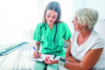 A senior caregiver checking the vitals of an elderly woman at home.