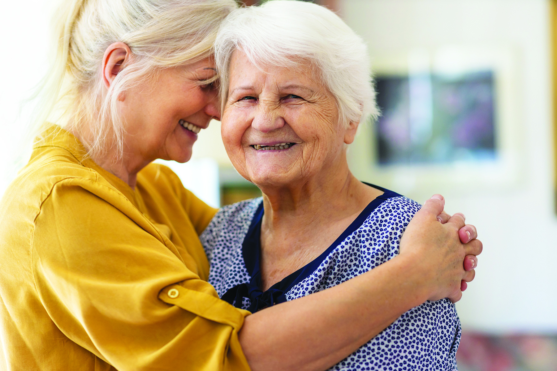 A caregiver hugging an elderly woman, both smiling.