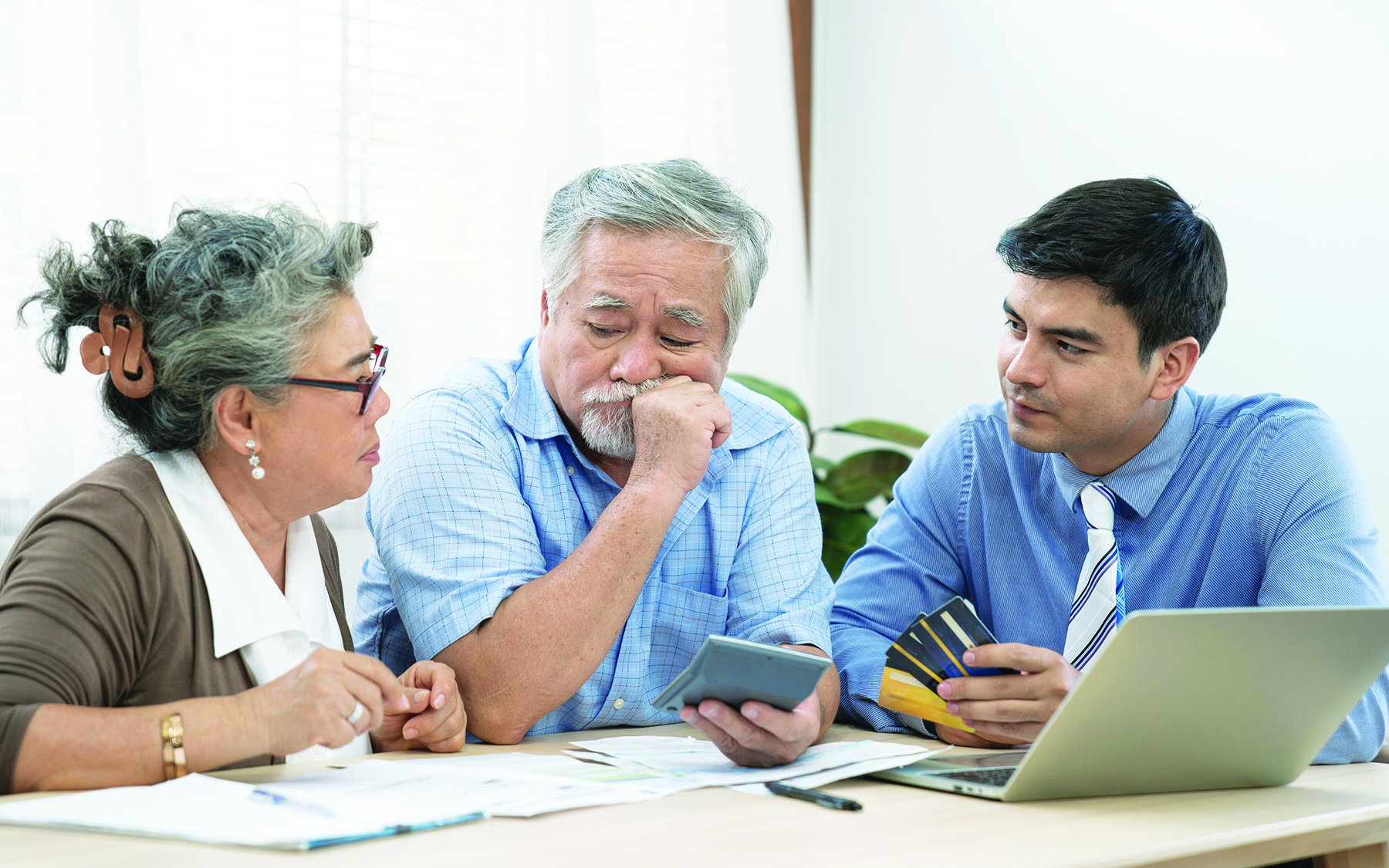 Two elderly individuals and an aging lifecare professional sit together at a table, reviewing documents and an open laptop, discussing aging care options and support services.