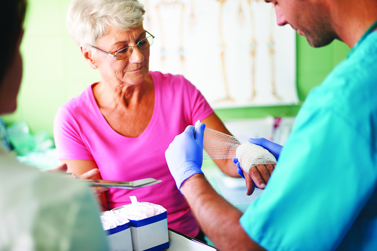 Healthcare providers treating a hand wound on an elderly woman.